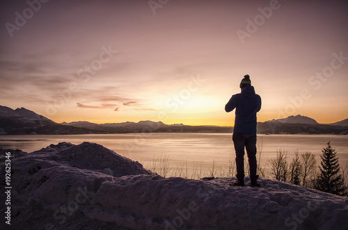 Silhouette of Person by Lake and Snow Covered Landscape at Sunset