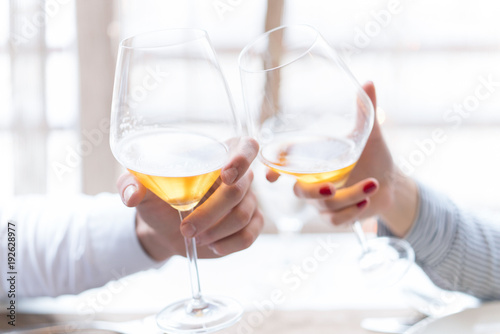 Close up portrait of a female and male hands toasting with glasses of white wine over table