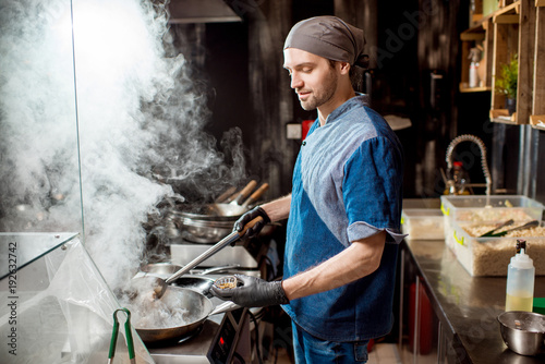 Caucasian chief cook cooking with wok pan on the asian restaurant kitchen