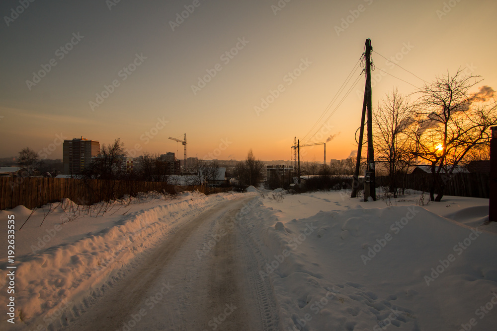 Snow-covered rural street lit by the setting sun