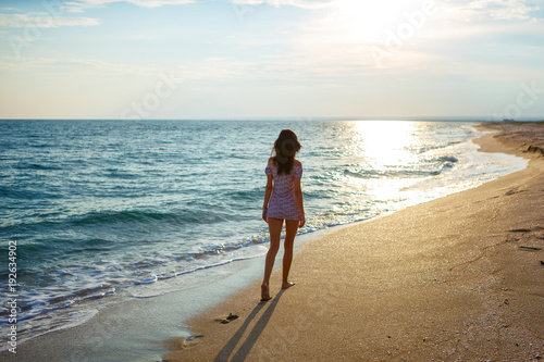 Young woman walk on an empty wild beach towards celestial beams of light falling from the sky, the concept of travel and tourism, leisure at sea