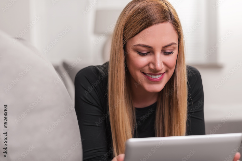 Attractive woman using a tablet pc while lying on the couch at home. Attractive woman using a tablet pc while lying on the couch at home.