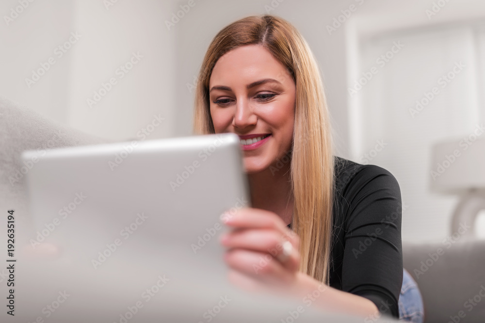 Attractive woman using a tablet pc while lying on the couch at home. Attractive woman using a tablet pc while lying on the couch at home.