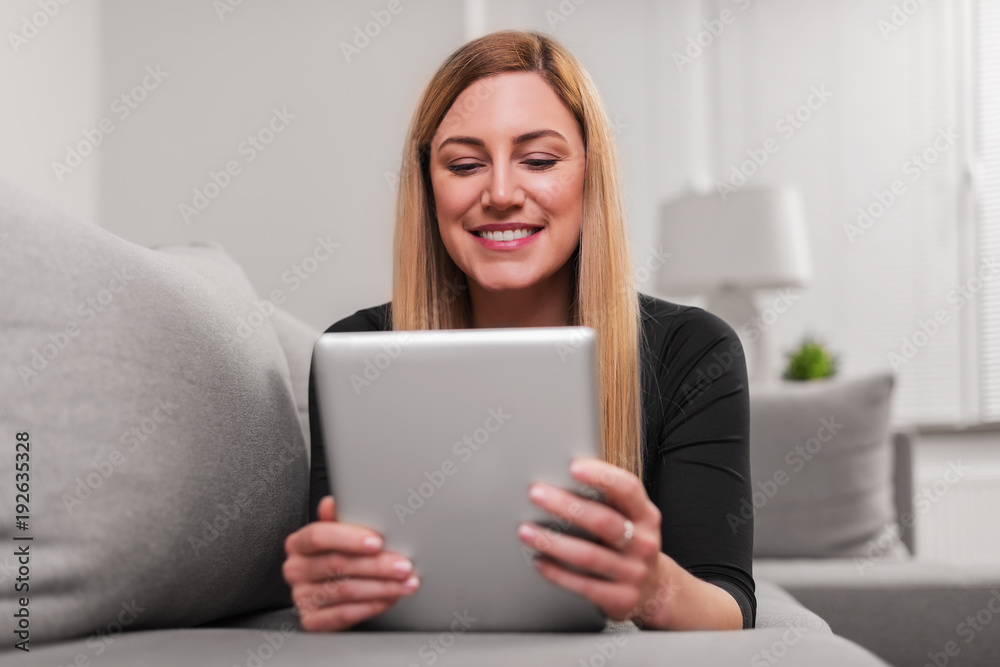 Attractive woman using a tablet pc while lying on the couch at home. Attractive woman using a tablet pc while lying on the couch at home.