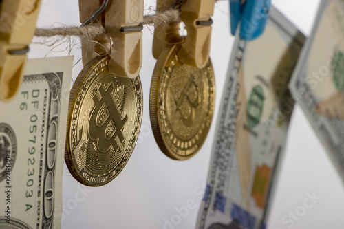 Money laundering concept. Yellow clothes peg hold Bitcoin and one hundred dollar banknotes photo