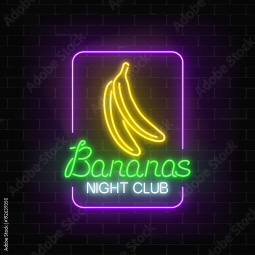 Glowing neon nightclub signboard with bananas in rectangle frame on dark brick wall background.