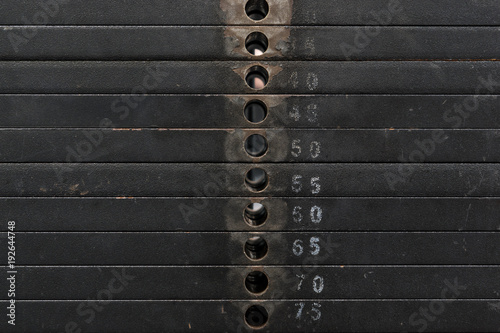 Old and used black weight stack with white numbers in a gym. Rusty flat metal weights.