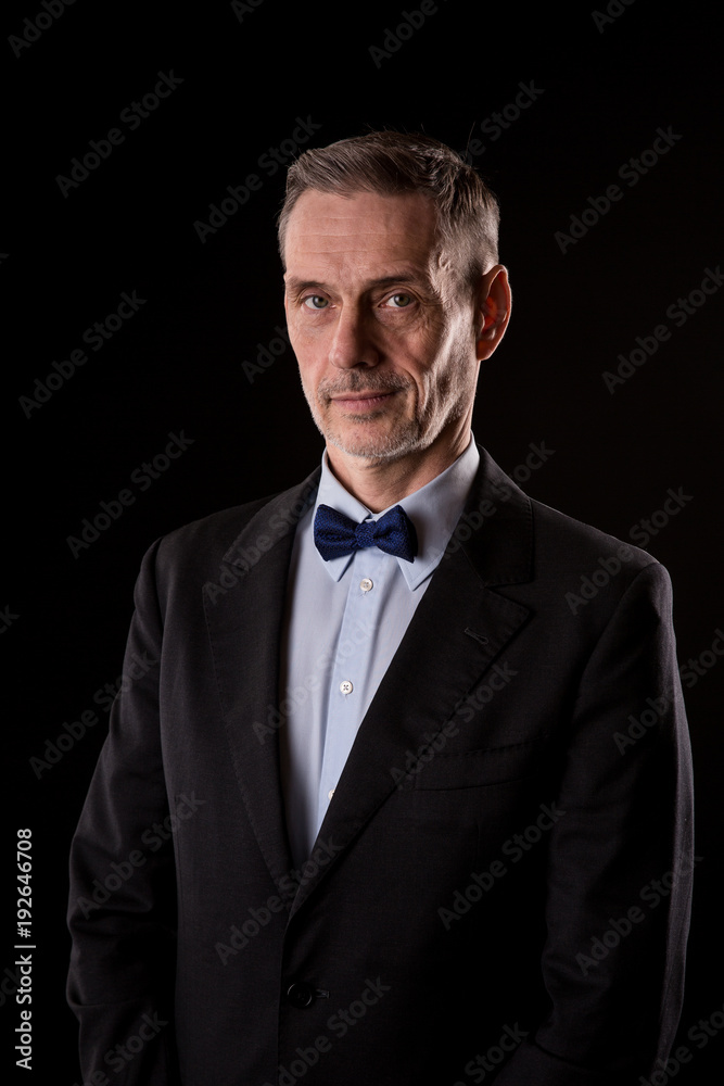 The older businessman in a suit with a bow tie on black background The older businessman in a suit with a bow tie on black background