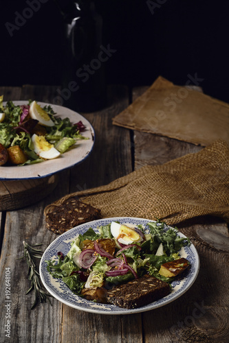 Potato salad with eggs, marinted onion, and grain mustard dressing served in two vintage plates. Old wooden background photo
