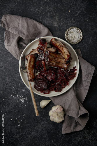Main dish with grilled pork ribs in thick barbeque sauce garnished with red cabbage and beets braised in red wine sauce. Dark textured background photo