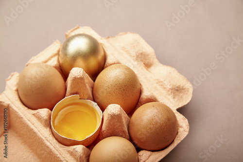 Half Dozen of chicken eggs in colorful cardboard container with one golden egg photo