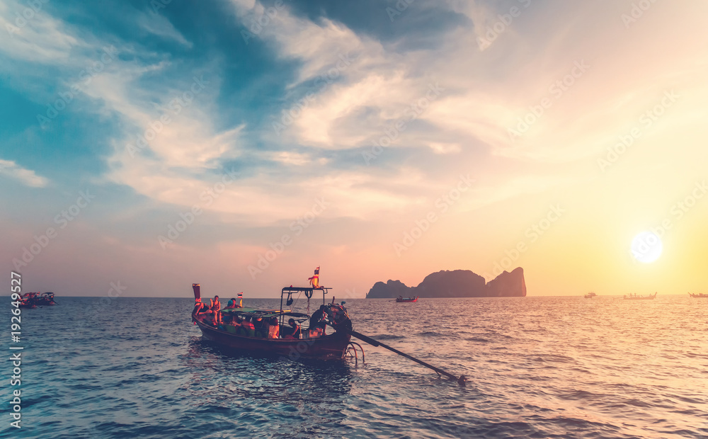 The traditional fishing boats with the tourists in the ocean next to the exotic Phi Phi Islands, the Kingdom of Thailand. Breathtaking colorful sunset background. Beauty of wild nature.