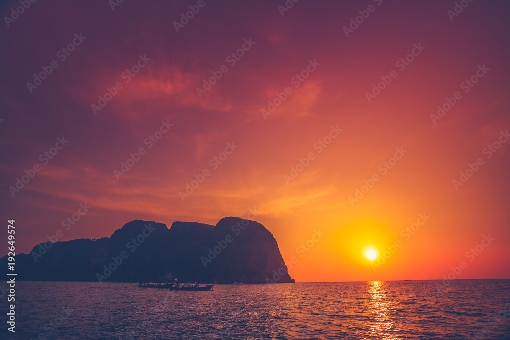 Breathtaking sunset over the ocean and limestone cliffs next to the exotic Phi Phi Islands, the Kingdom of Thailand. Amazing sky in the golden, orange and scarlet tints.