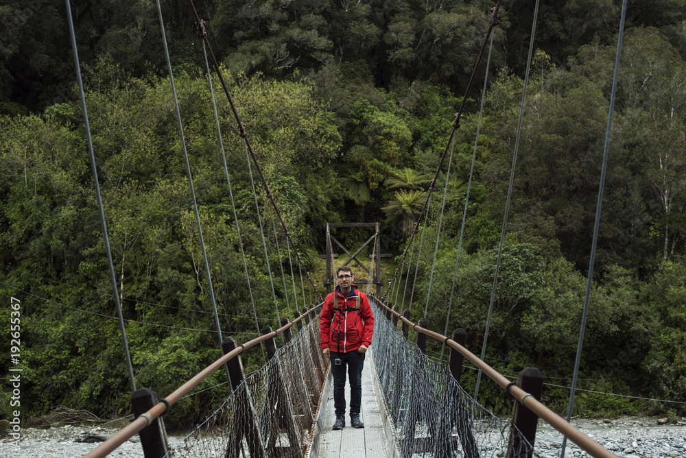 Hombre joven posando frente a un bosque en un puente de madera