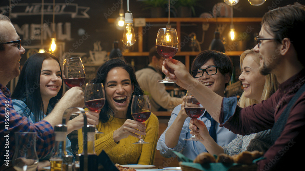 Diverse Group of Friends Celebrate with a Toast and Clink Raised Wine Glasses in Celebration. Beautiful Young People Have Fun in the Stylish Bar/ Restaurant. - obrazy, fototapety, plakaty 