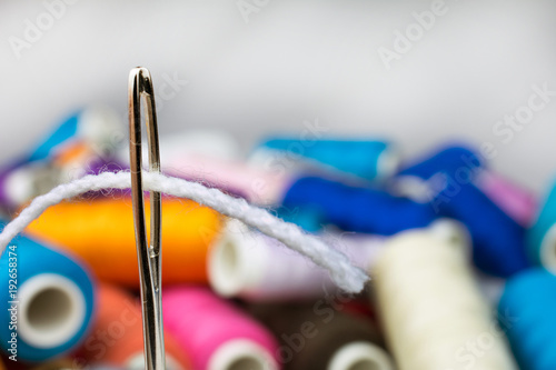 thread a white thread in a needle, a coil with a multicolored thread a blurred background