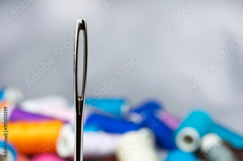 thread a white thread in a needle, a coil with a multicolored thread a blurred background