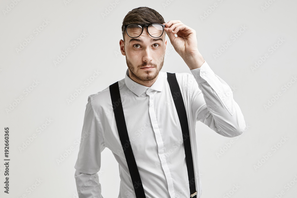 Human facial expressions and emotions. Portrait of emotional fashionable young bearded Caucasian male dressed in formal wear lifting his stylish eyeglasses, having confused questioning look Human facial expressions and emotions. Portrait of emotional fashionable young bearded Caucasian male dressed in formal wear lifting his stylish eyeglasses, having confused questioning look