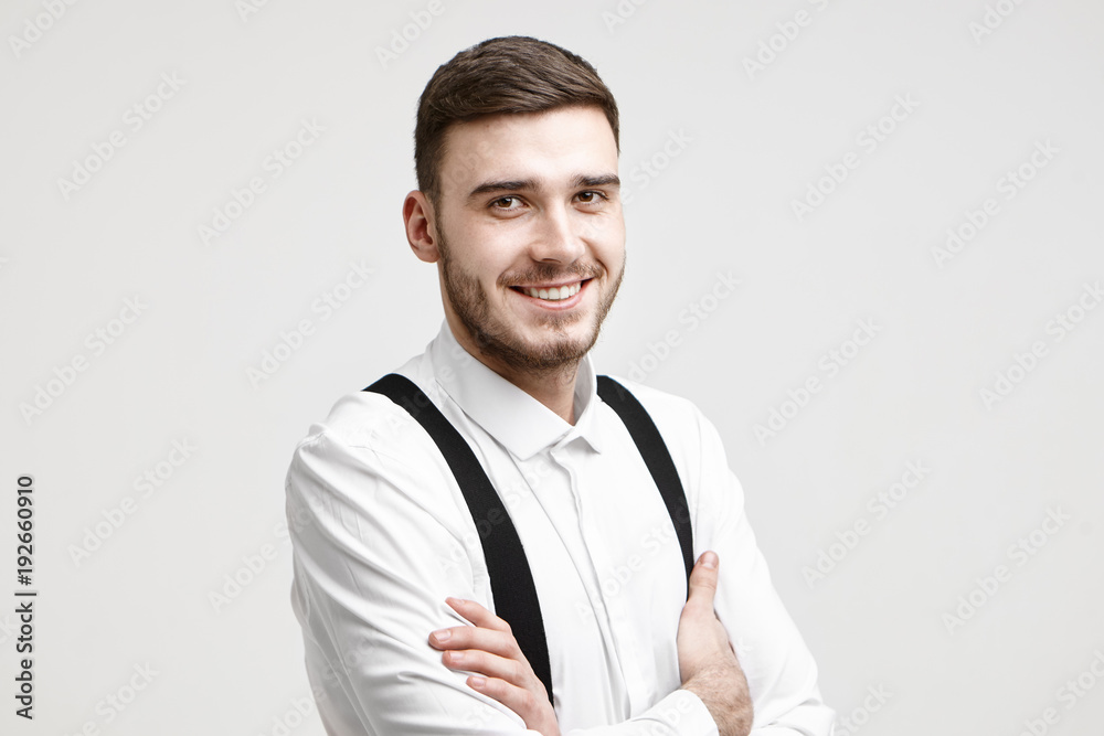 Horizontal shot of happy successful young entrepreneur with bristle and stylish haircut smiling confidently, folding arms, his look and posture expressing confidence, success and determination Horizontal shot of happy successful young entrepreneur with bristle and stylish haircut smiling confidently, folding arms, his look and posture expressing confidence, success and determination