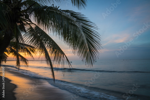 Beautiful sunset above the sea with views of palm trees on white beach