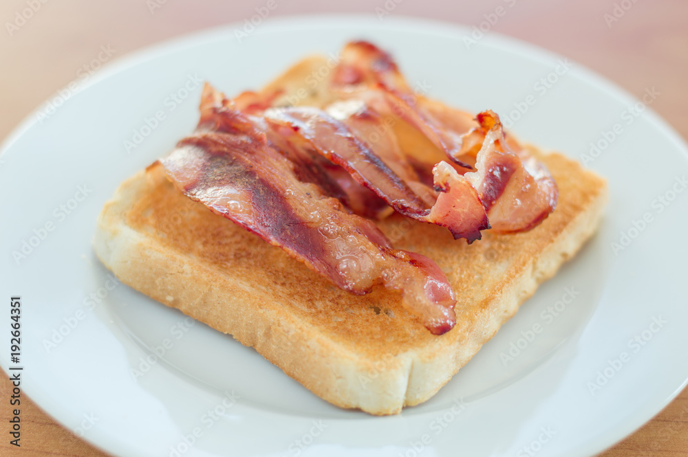 Fried bacon on toast on white plate.