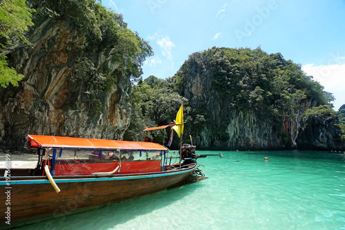 Longtail boat docked on an island in Thailand with rocky cliffs and aquamarine water photo