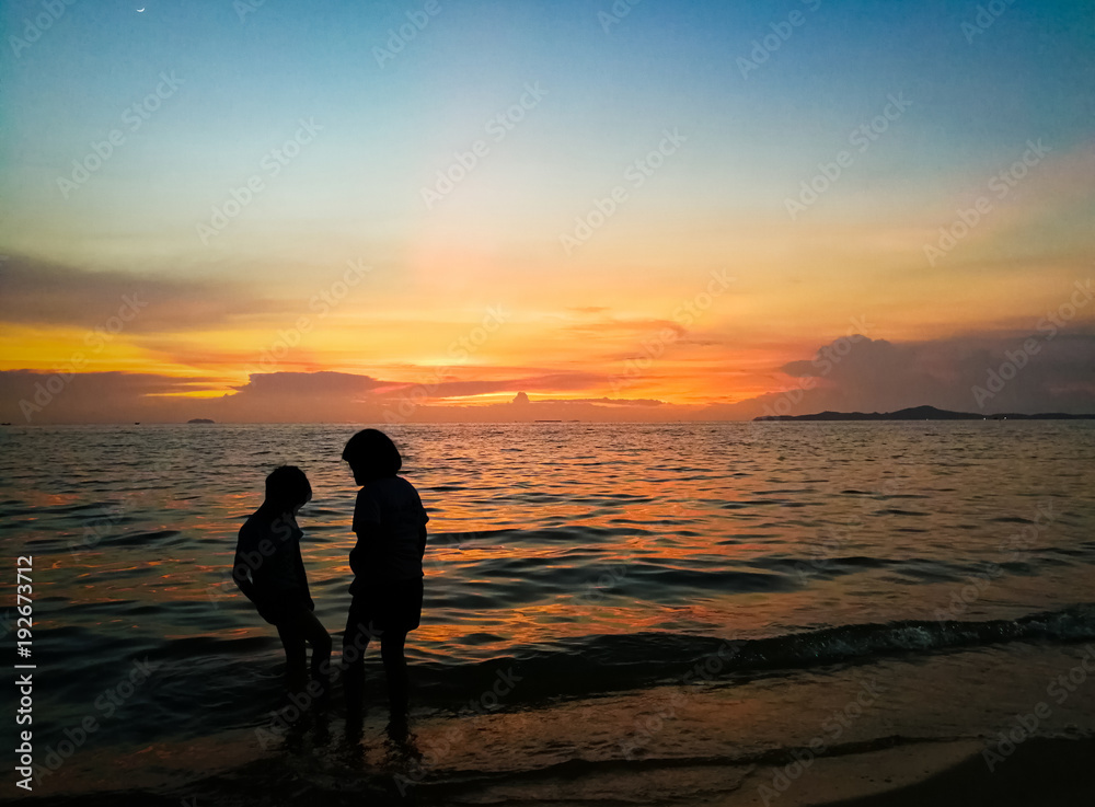 Beautiful of  The silhouette of a boy and a girl playing sea water at the beach at sunset.