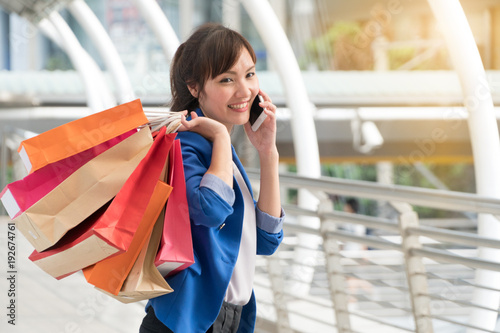 Beautiful young woman holding shopping bags and talking cell phone walking on shopping street background. Lifestyle shopping concept.