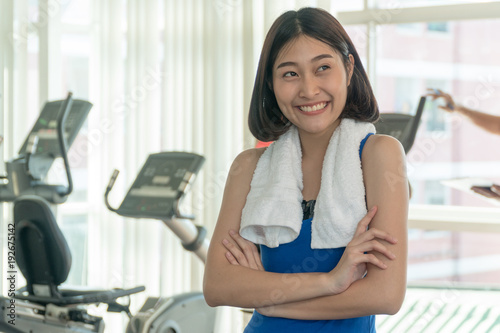 Portrait of a cheerful sports woman standing arms crossed in fitness gym.Beautiful woman wearing blue sportswear smiling happily at gym in front of elliptical machines.