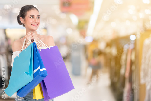 Smiling beautiful young woman holding many colorful shopping bags over Shopping malls background. happiness, consumerism, sale and people concept.