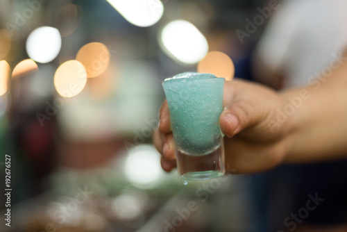 Hand hold cold Blue Maitai cocktail with bokeh blur light background