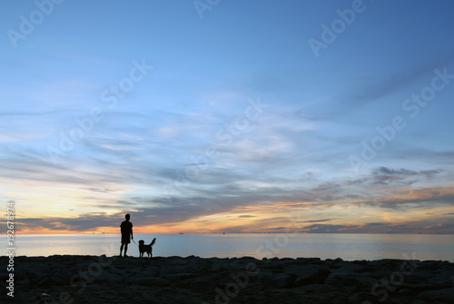 Silhouette a man with a dog on the beach at sunrise in the south of Thailand.Golden retriever silhouette on the beach.Travel with dog. © Nattapach