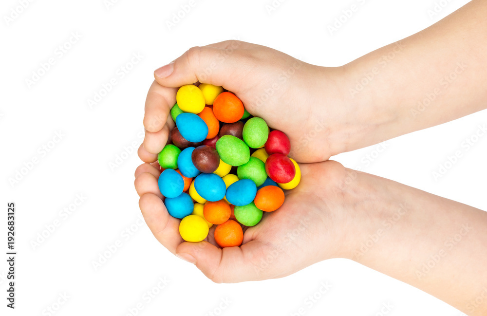 Child holding many colorful round candies in her palms. Isolated on white. Top view.