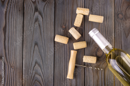 Glass bottle of wine with corks on wooden table background.