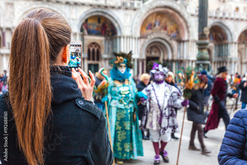 VENICE, ITALY - FEBRUARY 09 2018: Girl who takes the carnival masks in San Marco square with her cell phone