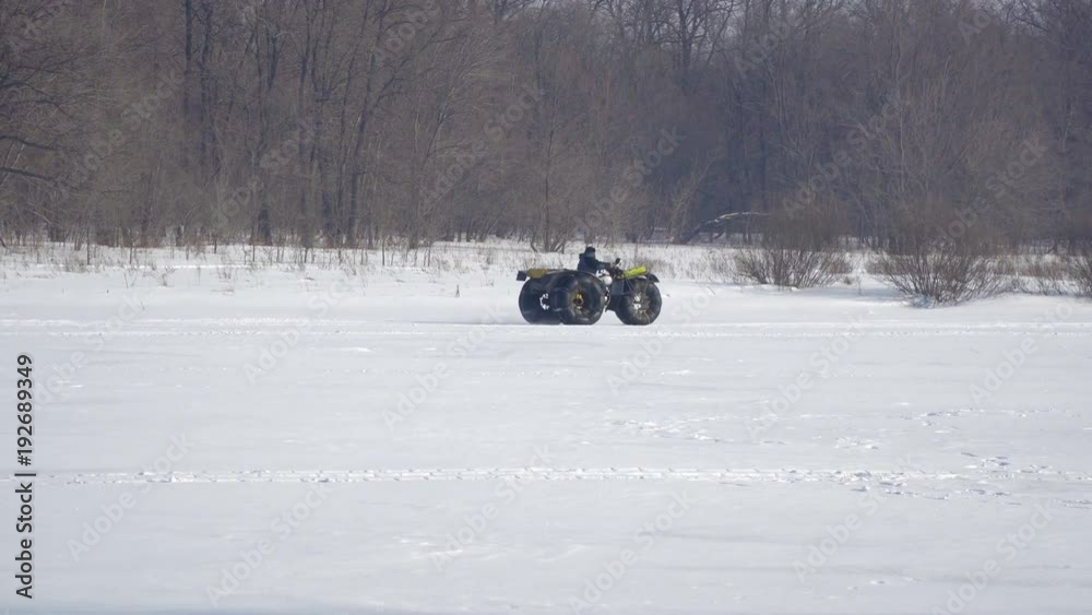 A man on a handmade motorcycle all-terrain vehicle with large wheels rides along the forest on snow A man on a handmade motorcycle all-terrain vehicle with large wheels rides along the forest on snow