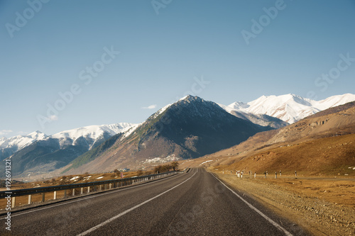View of the autumn road leading to the mountains to the snow-capped peaks of the Caucasus. The concept of traveling to the mountains by car
