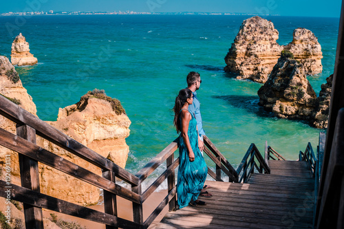 Happy young couple men and woman at the beautiful cliffs and rocky coastline of the Algarve by Lagos looking out over the ocean by praia di calimo,Praia dos Pinheiros