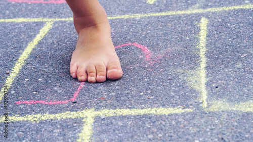 Closeup of little boy's legs and hopscotch drawn on asphalt. Child playing hopscotch game on playground outdoors.