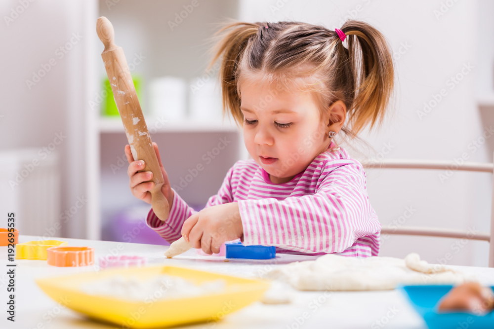 Little girl is playing and making cookies in kitchen. 