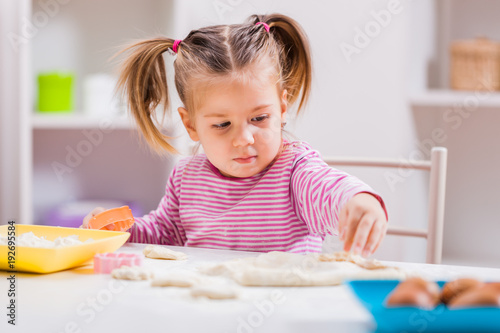 Little girl is playing and making cookies in kitchen. 
