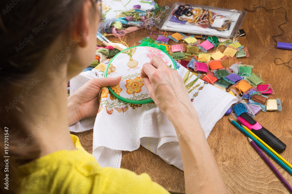 Girl sitting at a table where everything necessary for embroidery, embroiders a bigger picture Girl sitting at a table where everything necessary for embroidery, embroiders a bigger picture
