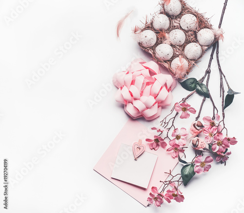 Pastel pink Easter composing with greeting card mock up with blossom decoration, feathers, eggs in carton box on white desk background, top view, flat lay