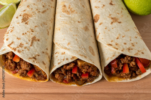 Tasty homemade burrito with vegetables and beef on wooden background.
