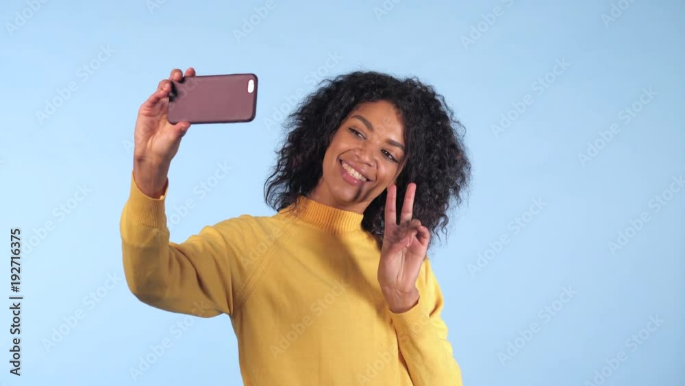 Beautiful african american woman holding and using smart phone to film herself in blue studio. Black female using technology networking on holiday, lifestyle. 4k Beautiful african american woman holding and using smart phone to film herself in blue studio. Black female using technology networking on holiday, lifestyle. 4k