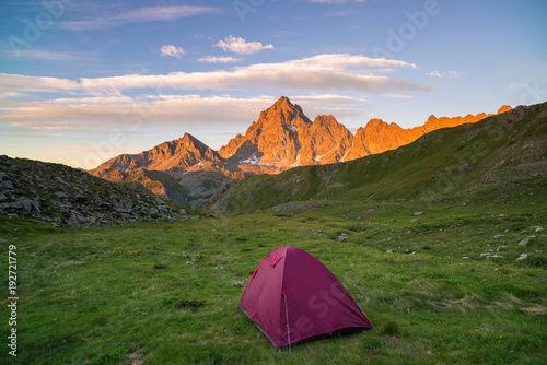 Camping with tent on the Alps.Snowcapped mountain range and scenic colorful sky at sunset. Adventure and exploration, conquering adversity.