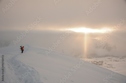 Snowboarder walking on the high mountain peak under the sun rays