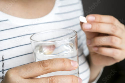 Close up image of woman putting white round pill in mouth. Sick female taking medicines, antidepressant, painkiller or antibiotic. Young lady drinking contraceptives. Pharmacy and healthcare concept