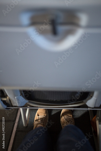 Passanger's legs squeezed between aircraft seats. Not too much space for legs.