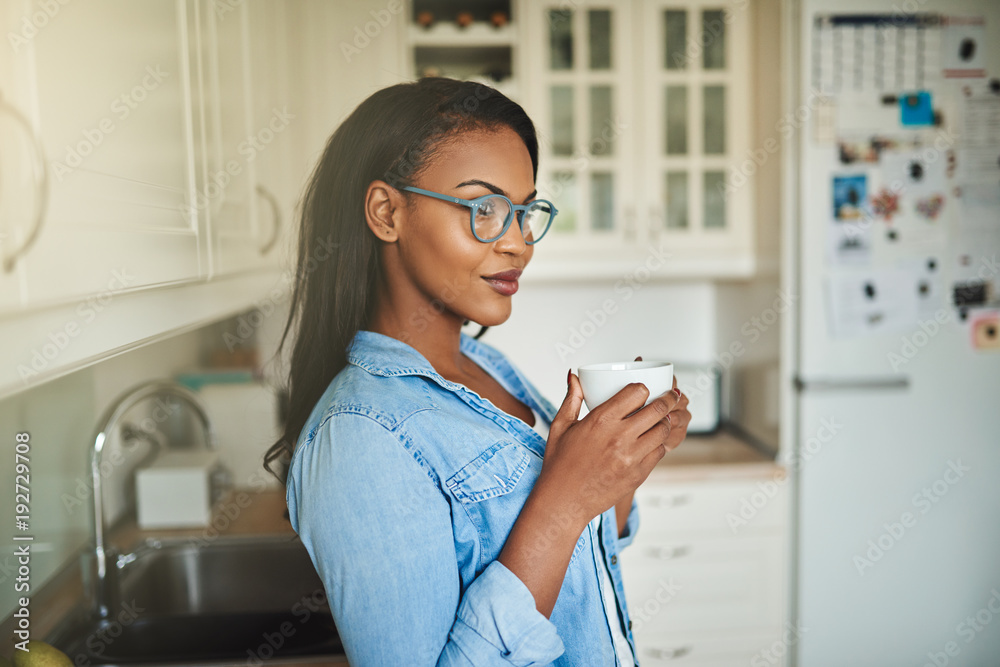 Young African woman standing in her kitchen with a coffee Young African woman standing in her kitchen with a coffee